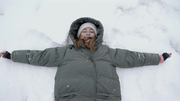 Top View Playful Young Woman Makes a Snow Angel on the Snow and Throws a Snowball