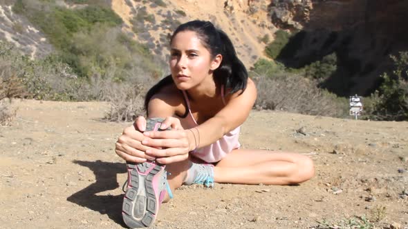 A young woman runner stretching before going on a trail run.