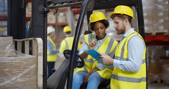 African Female Fork Lift Truck Driver Discussing Checklist with Foreman in Warehouse