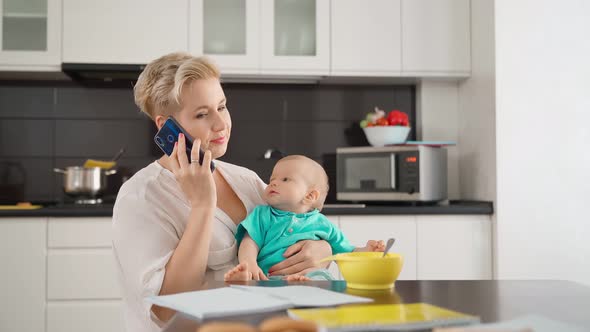 Woman Talking on Mobile While Sitting on Kitchen with Baby