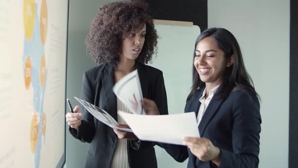 Young Beautiful Businesswomen Discussing Report and Smiling