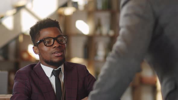 Black Businessman Shaking Hands and Speaking with Colleague in Restaurant