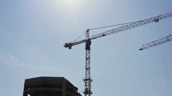 Aerial View Silhouette of Tower Crane Backlit with Sunlight Working on Building Site