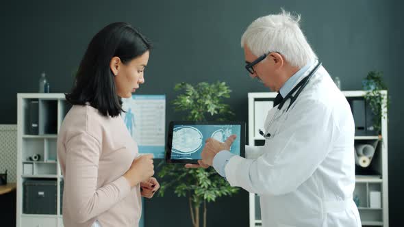 Doctor Showing Mri Images To Female Patient Using Tablet Touching Screen Working in Office