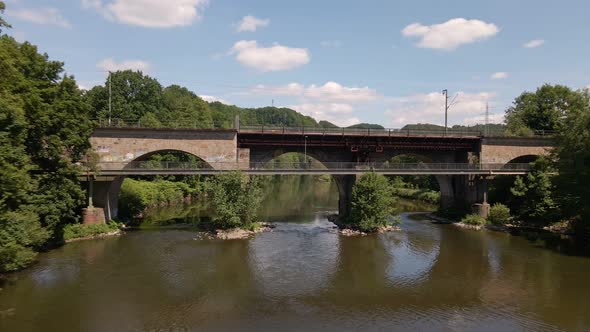 Aerial fly through shot of a stone train bridge within the lush nature of west Germany in spring.