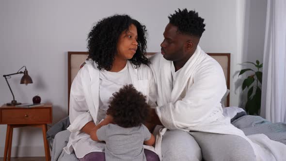 African American Man and Woman Sitting on Bed Talking and Little Boy Walking to Parents