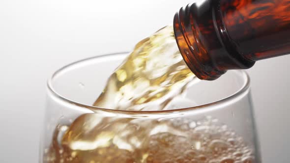 Beer is pouring with bubbles and foam in large beer glass from bottle on white background close up.