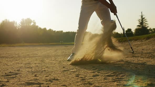 Golfer striking ball in sand