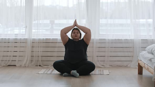 A Fat Woman Sitting in the Lotus Position and Doing Yoga at Home