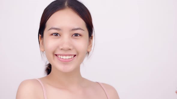 Slow motion of Asian girl with natural make up looking to camera and patting her body gently.