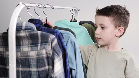 Boy preschooler standing by the hangers, racks up clothes, and chooses clothes for today.