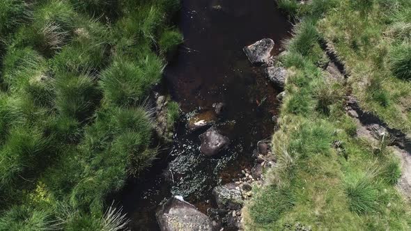 Birdseye close up aerial tracking forward of a rocky river following downstream surrounded by grassy