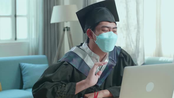 Asian Man Wearing Protection Face Mask And A Graduation Gown And Cap Having Video Call