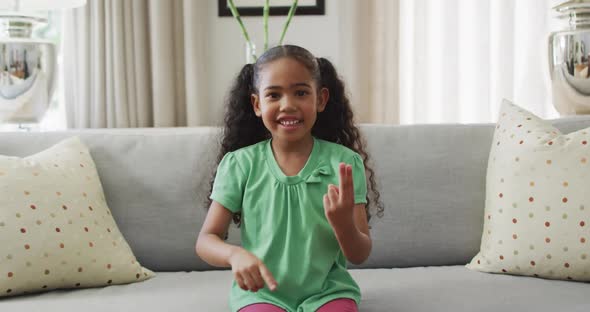 Happy biracial girl sitting on sofa using sign language