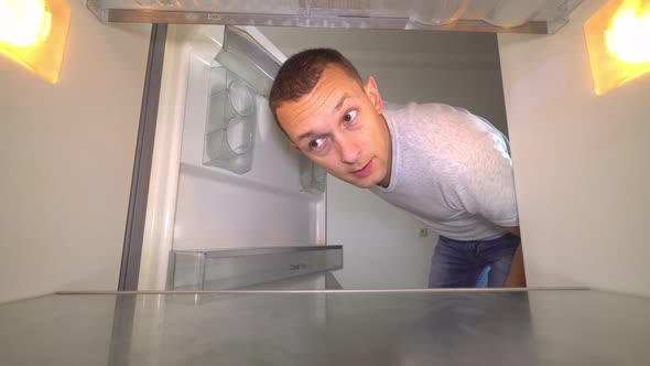 the man opens the refrigerator, sniffing and plugging his nose