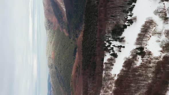 Aerial vertical format video of light snow covering forest covered hills