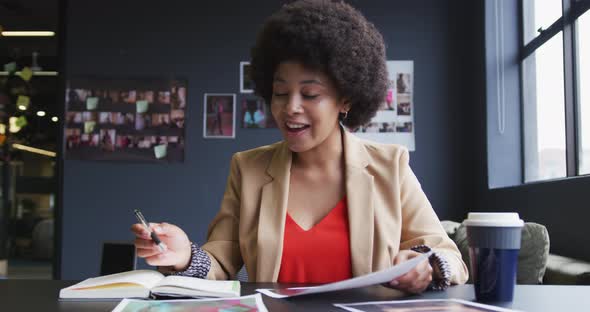 Mixed race businesswoman sitting having a video chat going through paperwork in a modern office