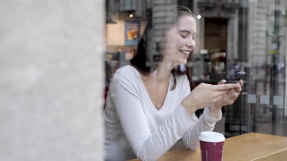 Young woman in a cafe enjoying a coffee and using a smartphone