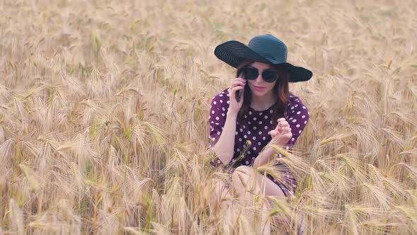 Beautiful Young Hippie Woman in the Wheat Field at Sunset Uses a Smartphone