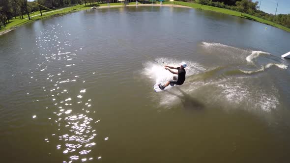 Aerial drone shot of a man riding his wakeboard at a cable park.