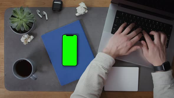 A Man is Typing on a Laptop at a Desktop with Mobile Phone Lying Next to It