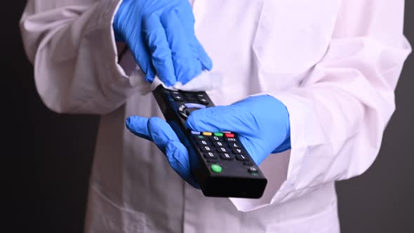 a Man in a Robe and Gloves Disinfects a TV Remote. Virus Protection, Obesity To Get Infected