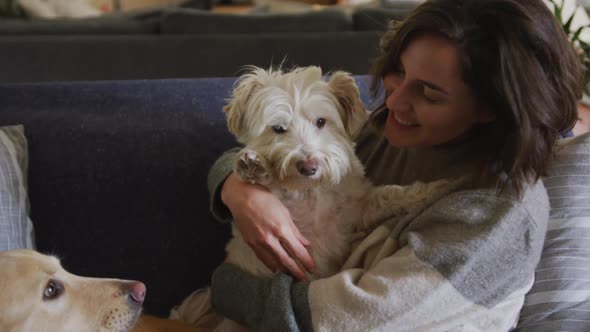 Smiling caucasian woman cuddling her pet dog sitting on sofa at home