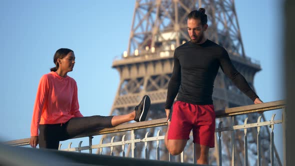 A couple stretching before running across a bridge with the Eiffel Tower