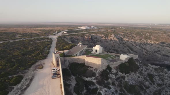 Drone hovering toward cliffside fortress and chapel - Fort of Santo António de Belixe Sagres