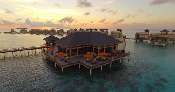 Aerial drone view sunset scenic tropical island, resort hotel with overwater bungalows, Maldives