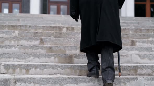 An Old Grandfather in a Black Coat Climbs the Stairs Walking Hard