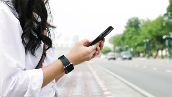 Close up hands young woman typing a message on a smartphone while standing beside the street.