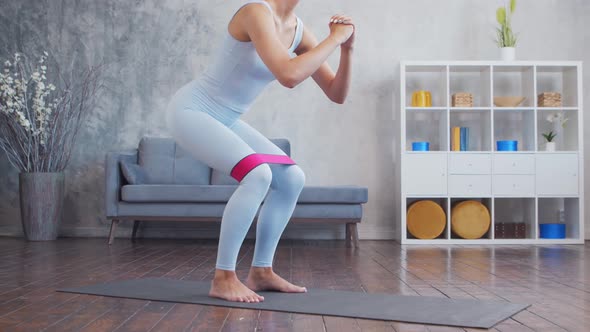 Young and sporty girl in sportswear is using resistance band while doing at home.