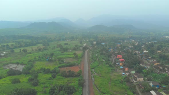 falling drone shot over rural Indian road hills background green