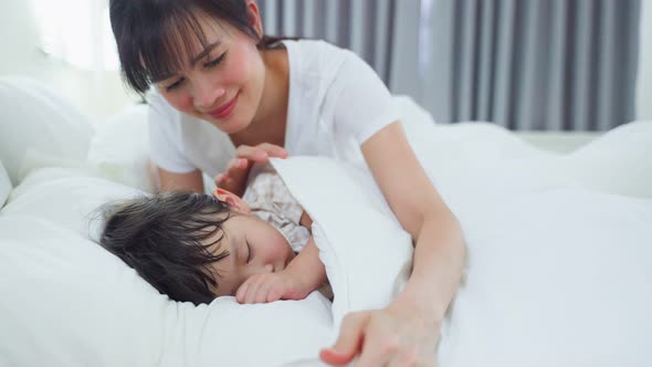 Asian caring parent mom put blanket on sleeping little small girl daughter on bed in the morning.