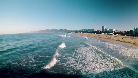 Point of View from pier of blue waves lapping onto California beach on sunny day