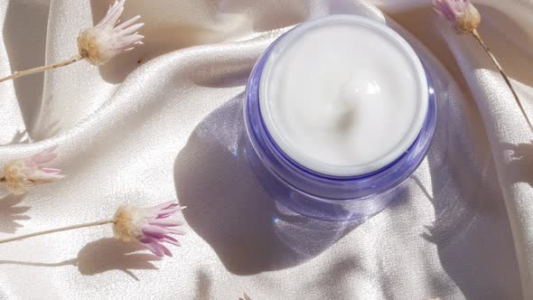 Blue glass cream jar on smooth silk background in sunlight with flowers shadow 4K skincare cosmetics