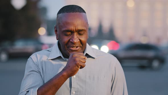 Mature African American Man of Retirement Age Standing on Street Outdoors Suffering From Cough