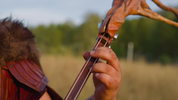 Folk Musician Presses Strings on Deck Playing Ikili on Field