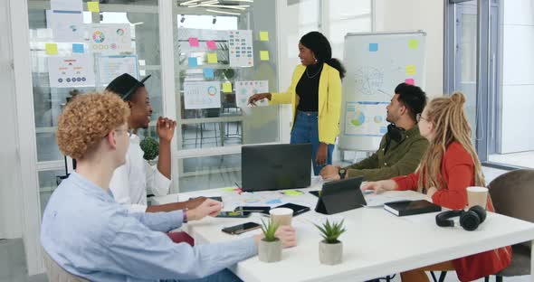 Motivated Diverse Team Discussing Strategy of Joint Project Using Infographics on Glass Wall