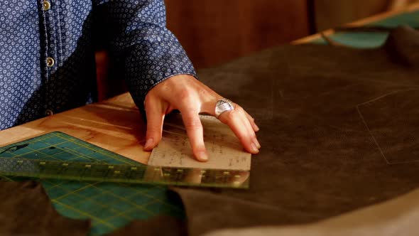 Mid-section of craftswoman measuring leather with scale