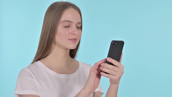 Young Woman Upset By Loss on Smartphone, Blue Background