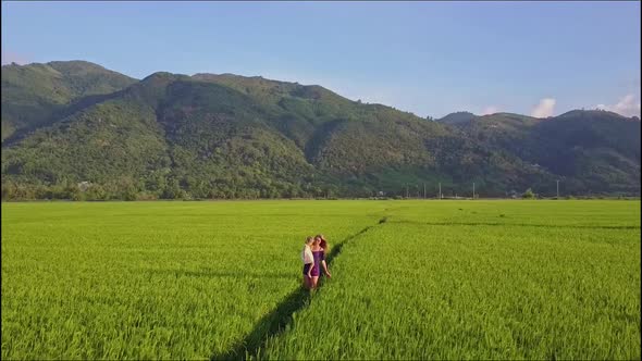Woman Carrying Girl Approaches Drone Camera Among Fields