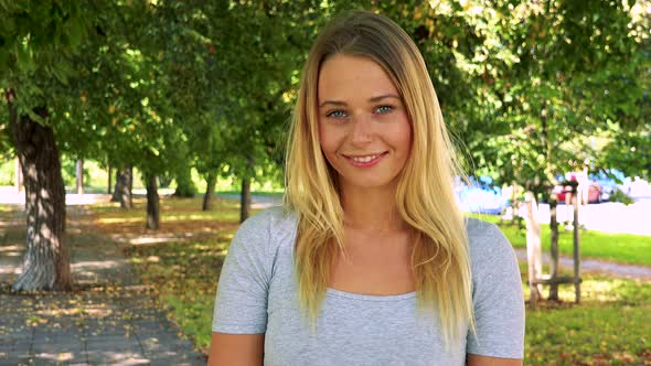 Young Pretty Blond Woman Smiles To Camera - Park with Trees in Background