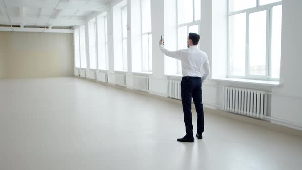 Businessman takes rented office space on smartphone, back view.