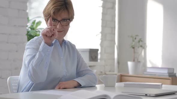 Old Woman Pointing with Finger at Camera at Workplace