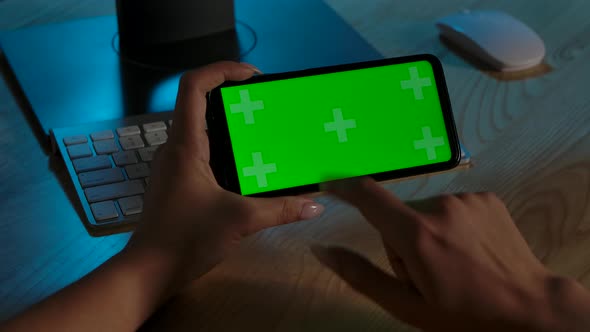 Rear View of Woman Holding Chroma Key Green Screen of Smartphone in Horizontal Position. She Scrolls