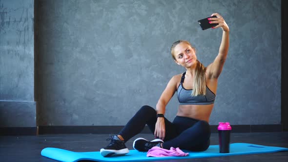 A Sports Woman Takes Photos on the Phone After a Workout in a Fitness Club