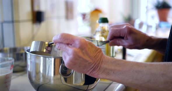 Hands of an elderly woman chef measuring and mixing ingredients in a bowl while baking a vegan choco