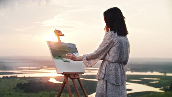 A Young Woman Artist Standing at Sunset and Drawing a Painting of Nature Landscape